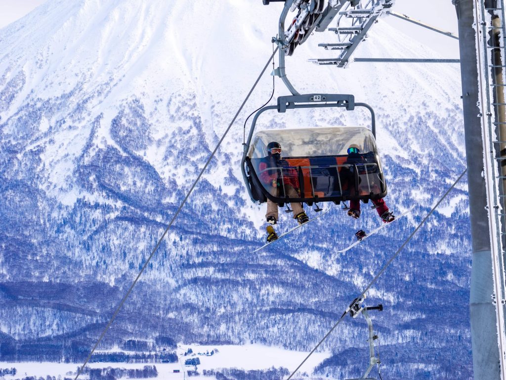 羊蹄山を背景にリフトに乗るスノーボーダー